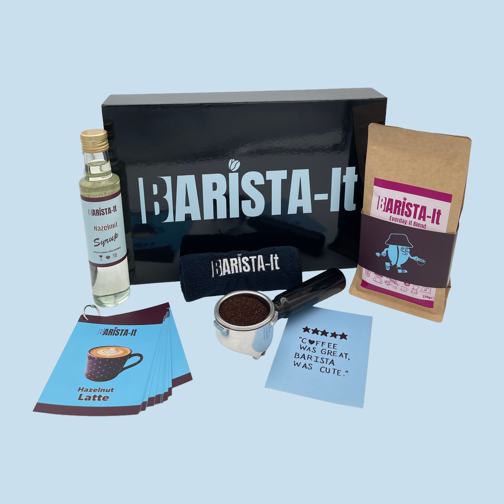 Collection of Hazelnut Barista-it Coffee products including a black box, Syrup bottle and recipe cards.