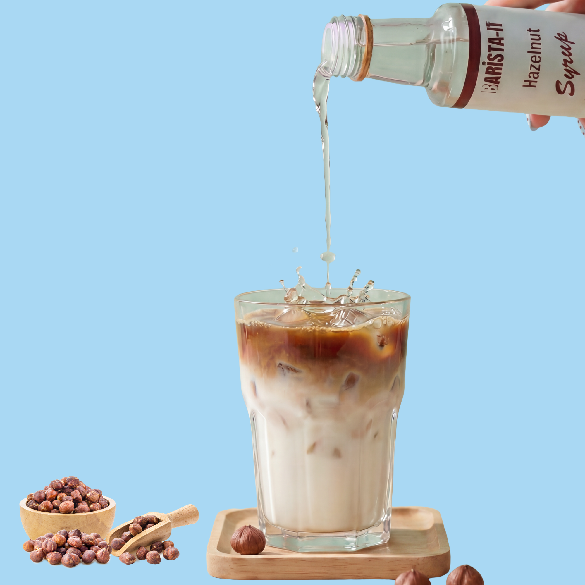 Bottle of hazelnut syrup being poured into a glass of iced coffee with hazelnuts on a blue background.