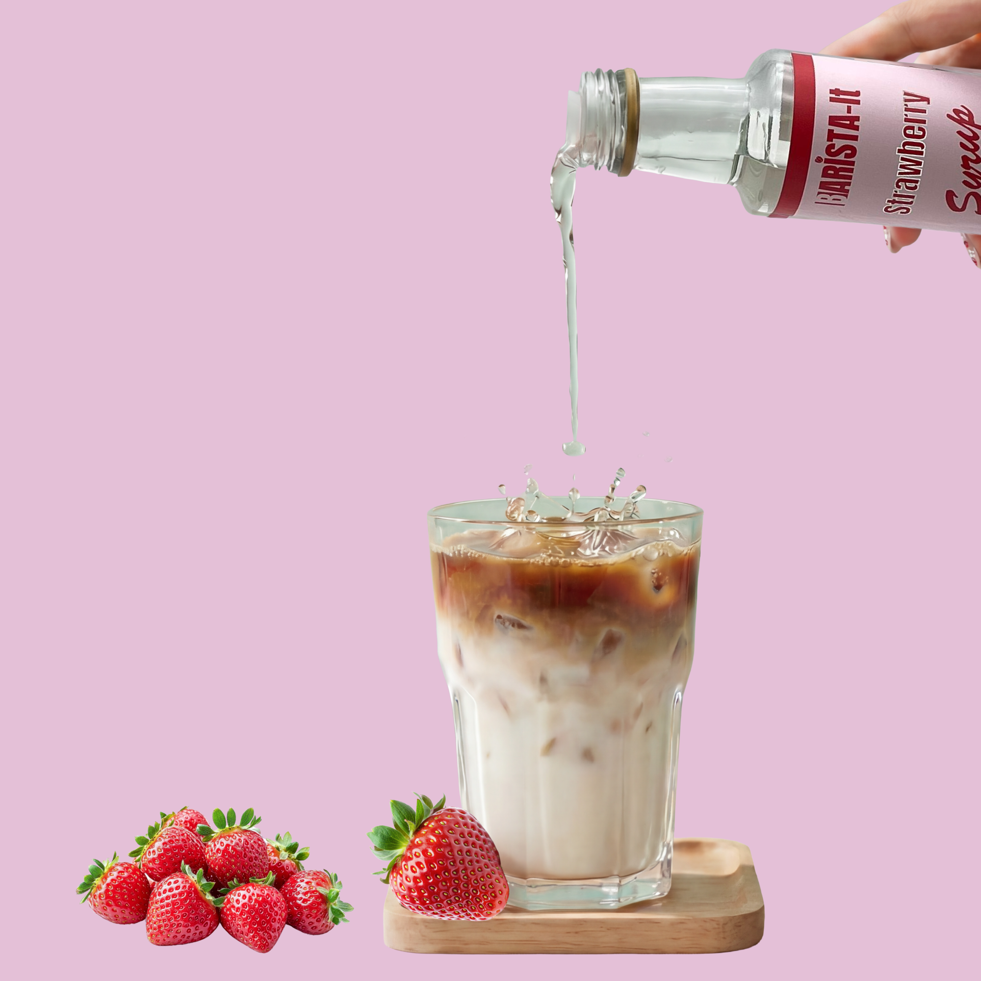 Bottle of strawberry syrup being poured into a glass of iced coffee with strawberries on a pink background